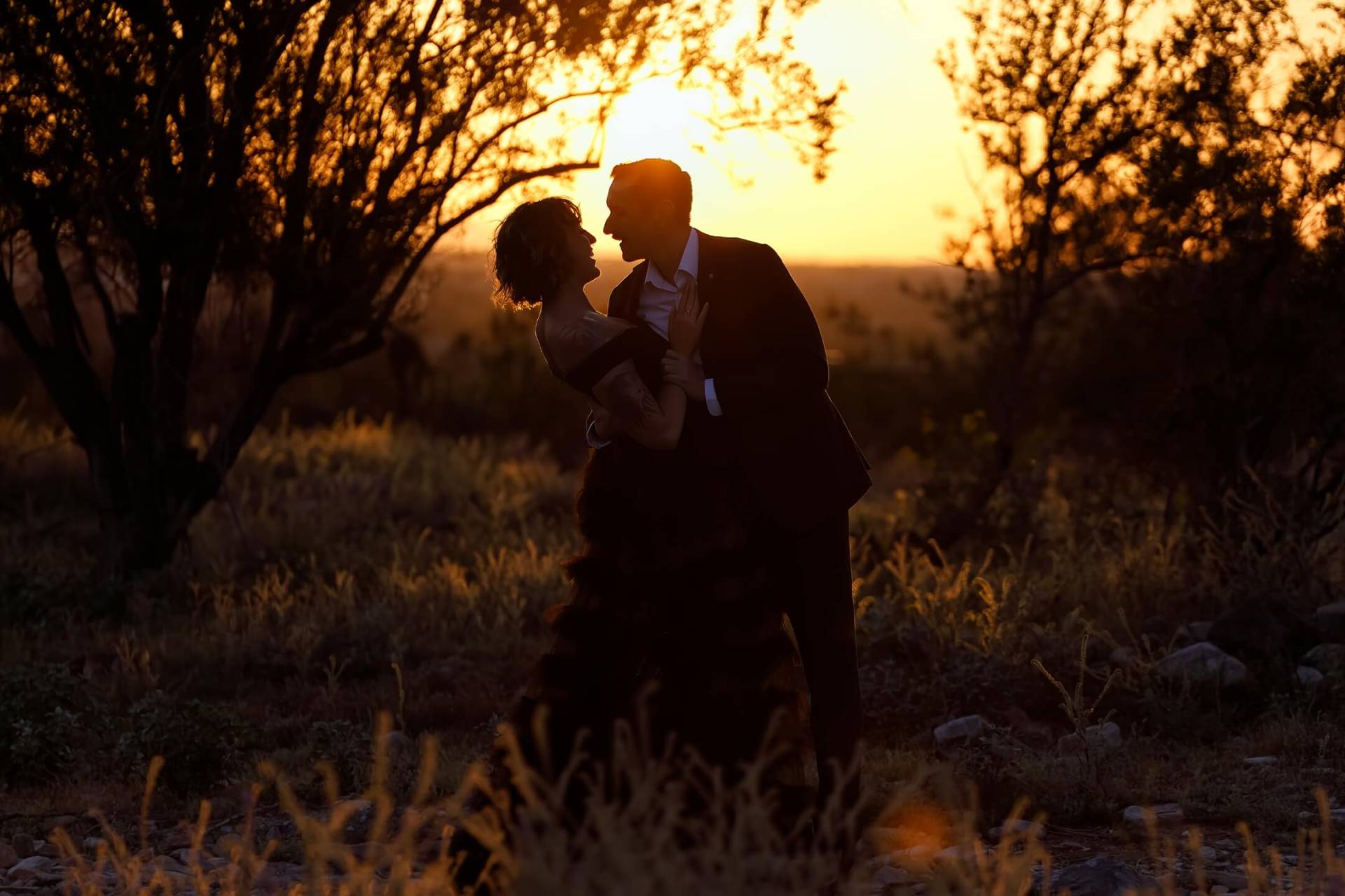 Dressed Up Couple in a Romantic Embrace About to Kiss with the Sunset Behind Them